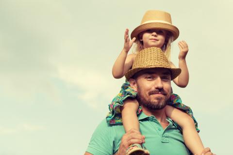 Father carries daughter on shoulders while outside on a sunny day