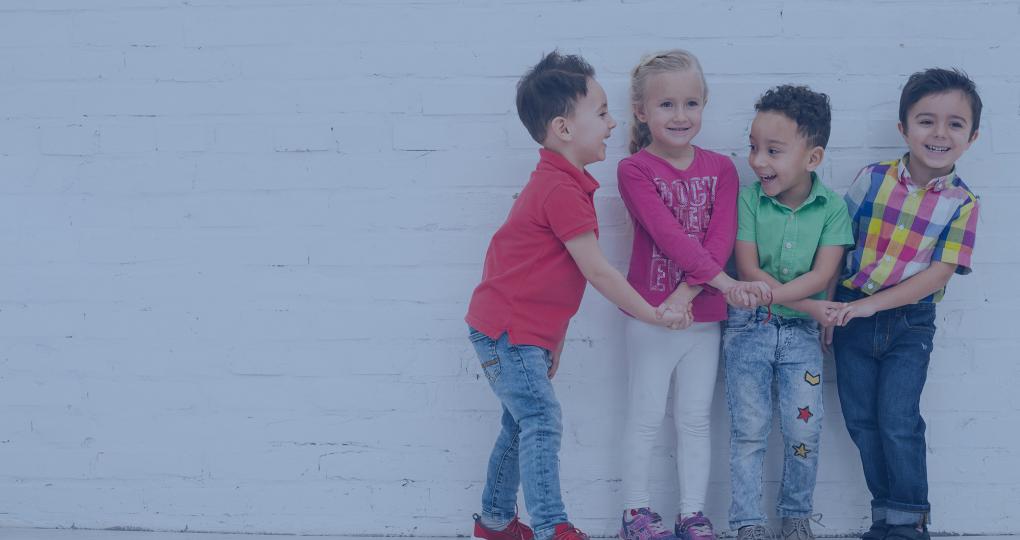 Four little kids hold hands while laughing.