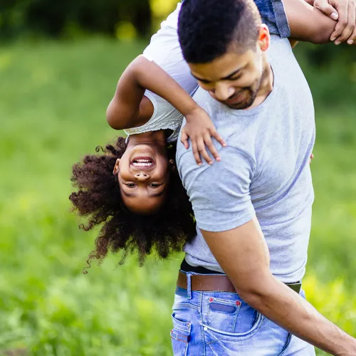 Father carries laughing daughter over his shoulder while playing outside