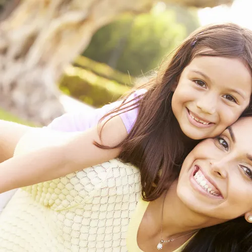 Smiling mother giving happy daughter a piggy back ride outside during the spring