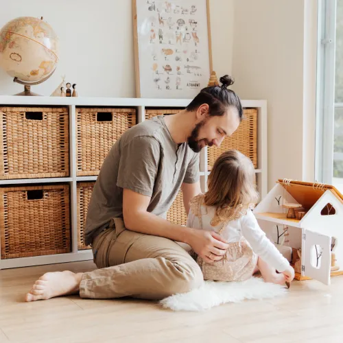 A father and his daughter play together with a doll house.