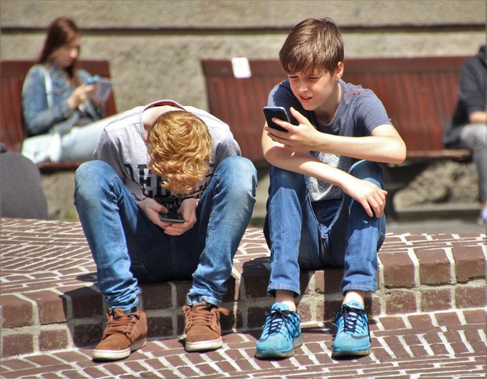 Two boys sit on a step and look at their smartphones.