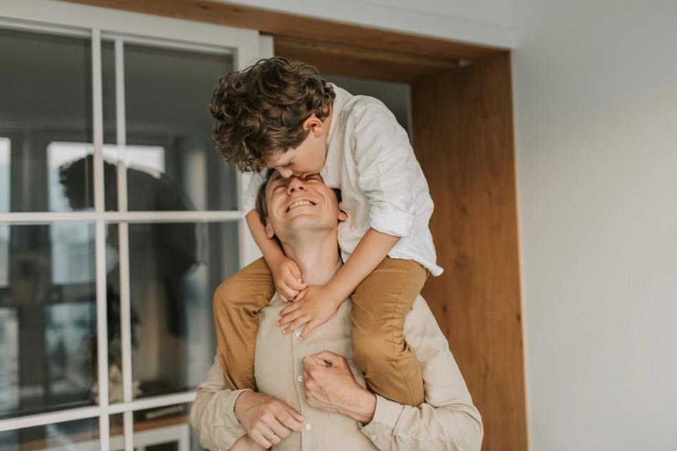A dad holds his son on his shoulders in the kitchen.