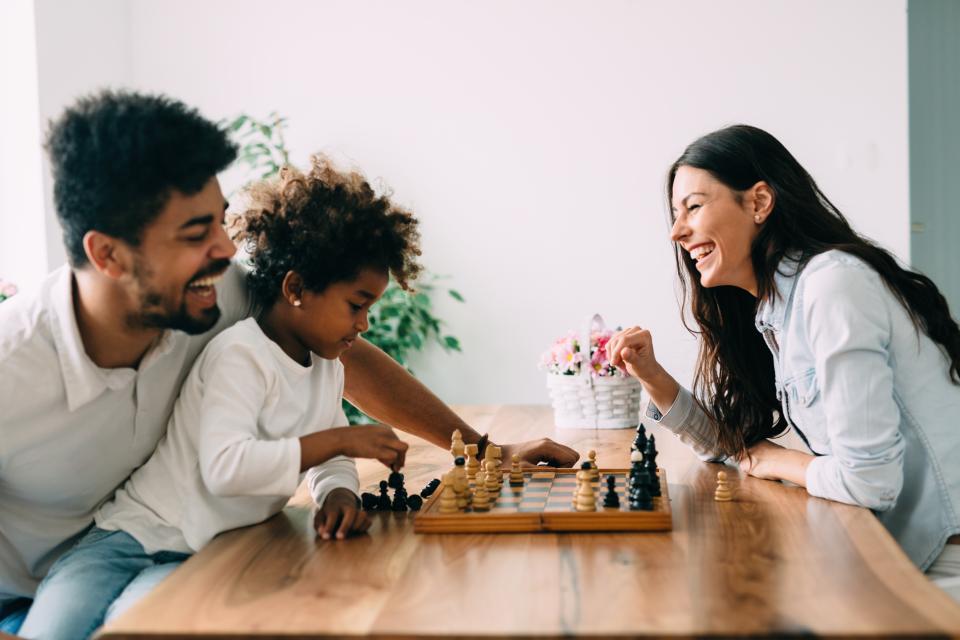 A woman plays chess with a man and his young daughter.