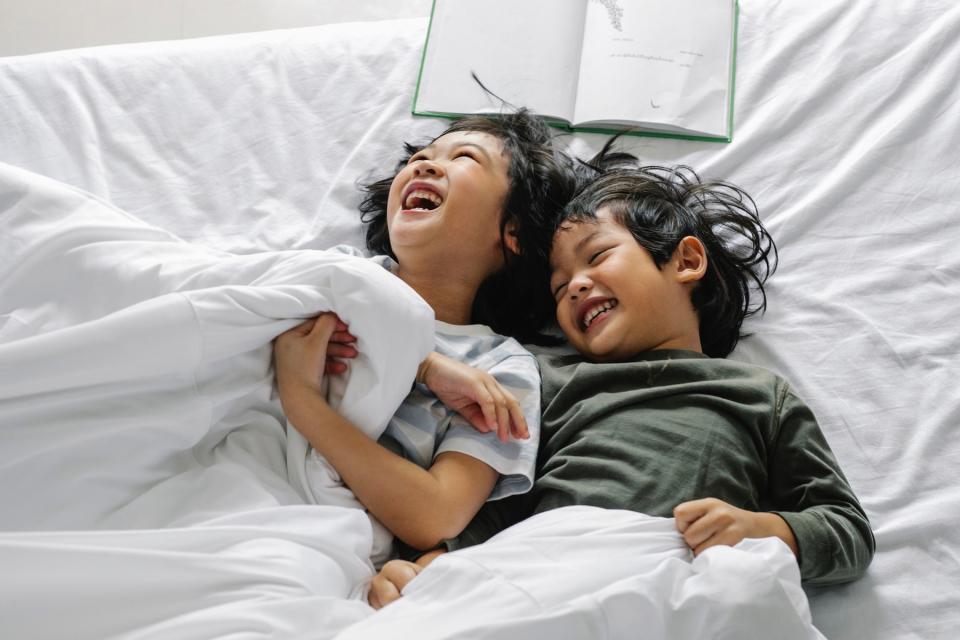 Siblings laugh together in bed.