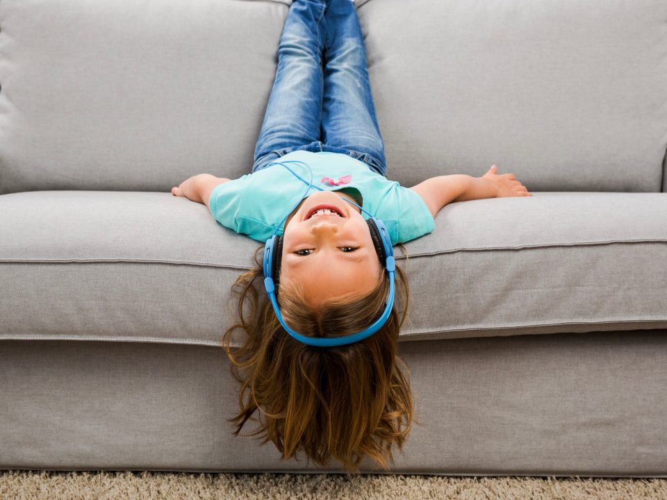 Girl laying upside on couch wearing headphones.